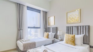Een hotelkamer met twee bedden, een groot raam met gordijnen, een nachtkastje met een lamp en twee ingelijste kunstwerken aan de muur.