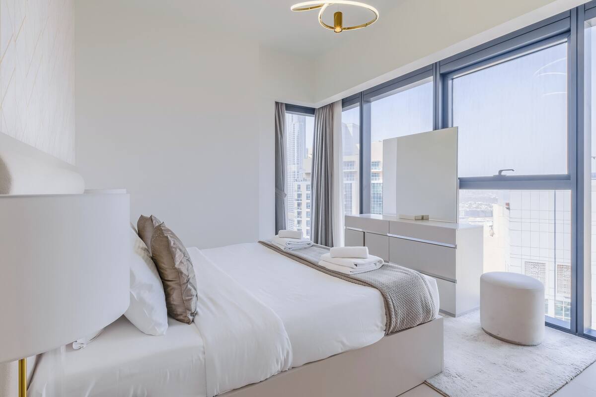 Ein modernes Schlafzimmer mit einem großen Bett, einem Schminktisch mit Spiegel und Blick auf die Stadt durch große Fenster.