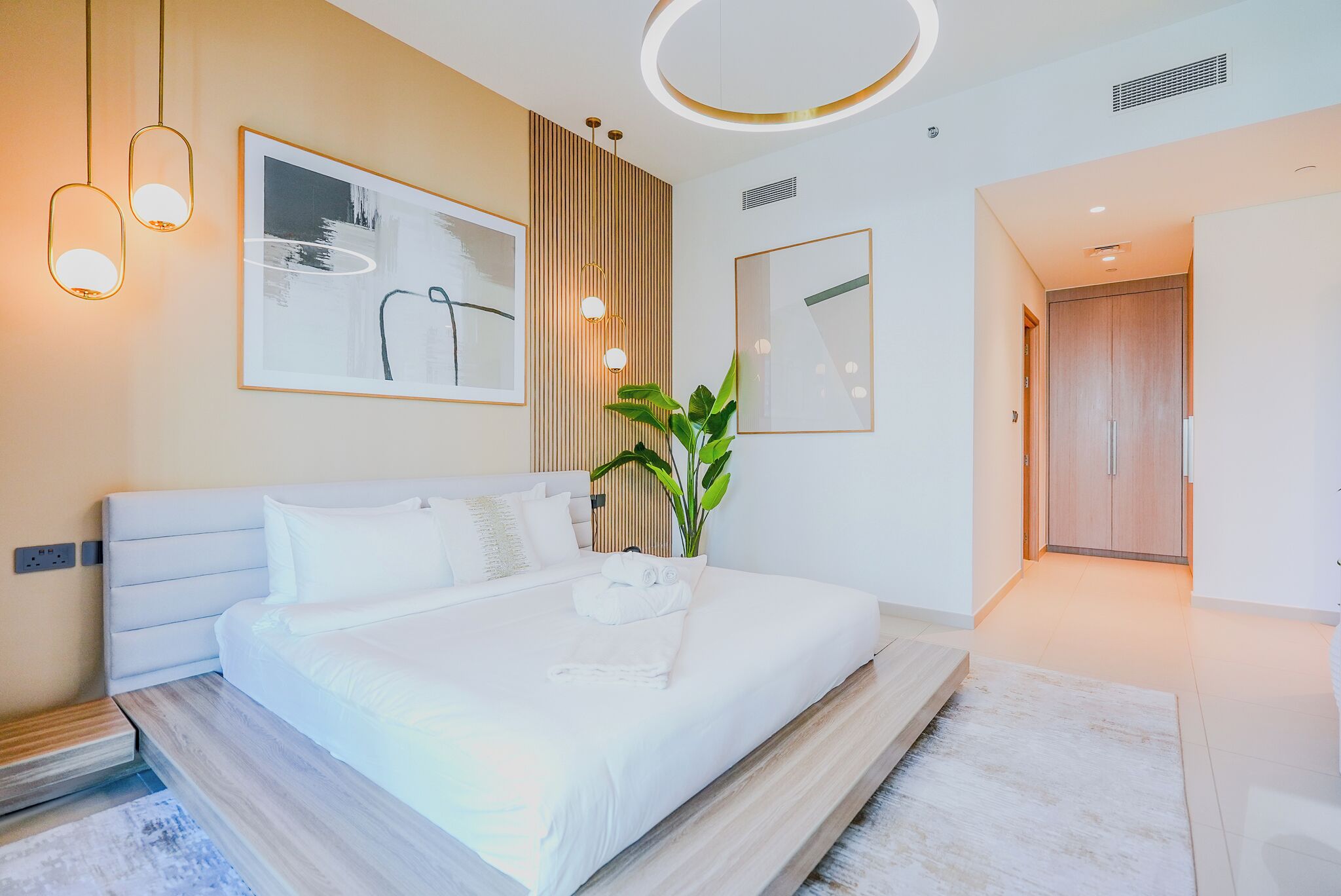 Ein modernes Hotelzimmer mit einem großen Bett, einer Topfpflanze und Bildern an den Wänden.