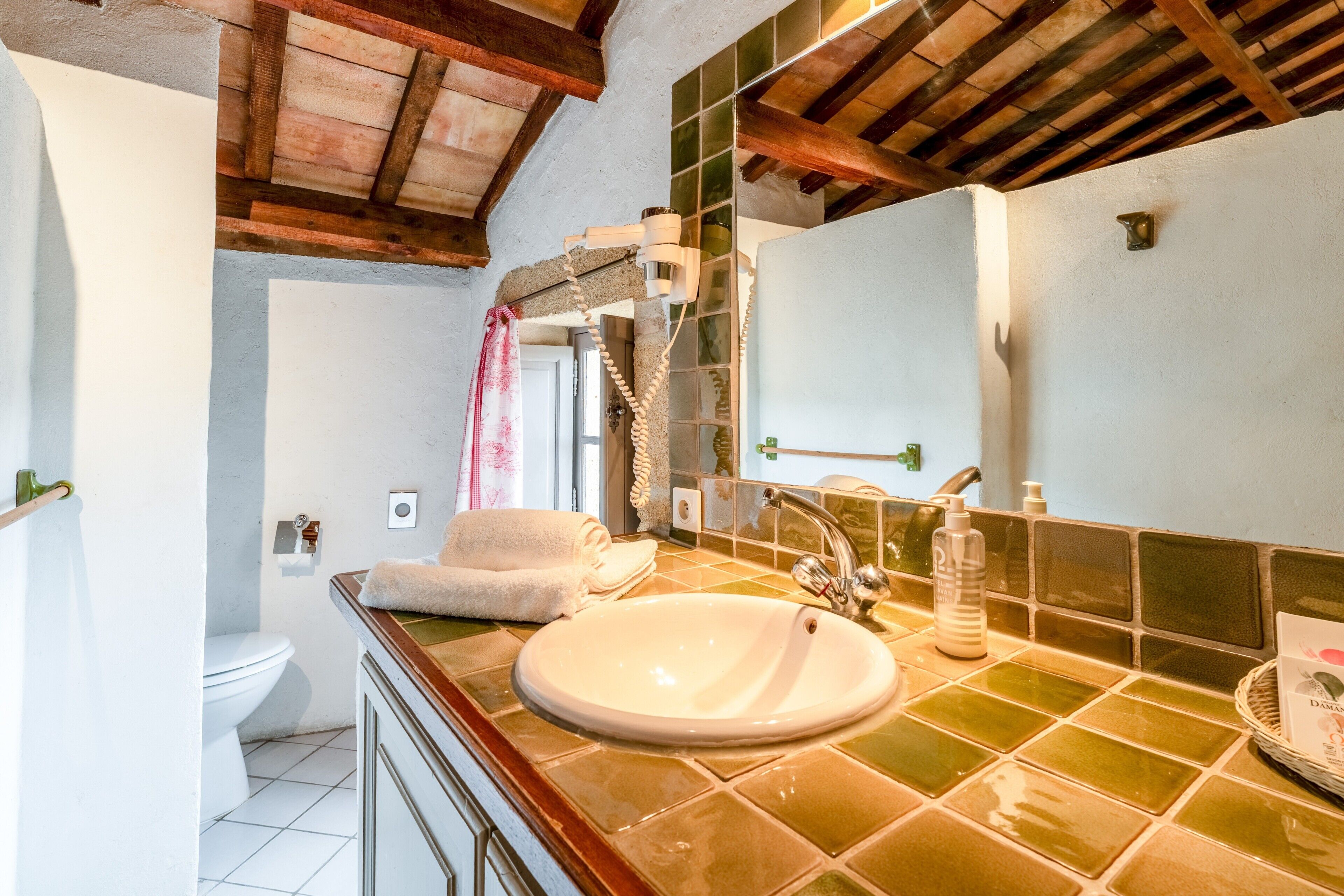 A bathroom with a white sink, green tiled backsplash, wooden ceiling beams, a mirror, and a towel rack.