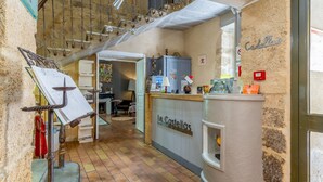 Un estrecho pasillo con piso de baldosas, un mostrador de recepción con el letrero 'Le Castellas' y una escalera con copas de metal colgantes.