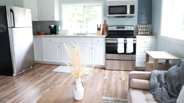 A modern kitchen with white cabinets, a black refrigerator, a microwave, and a stove. There is a vase with dried plants on the counter.