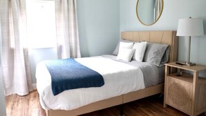 A neatly made bed with a blue blanket, a bedside lamp, and a small wooden nightstand with a mirror.