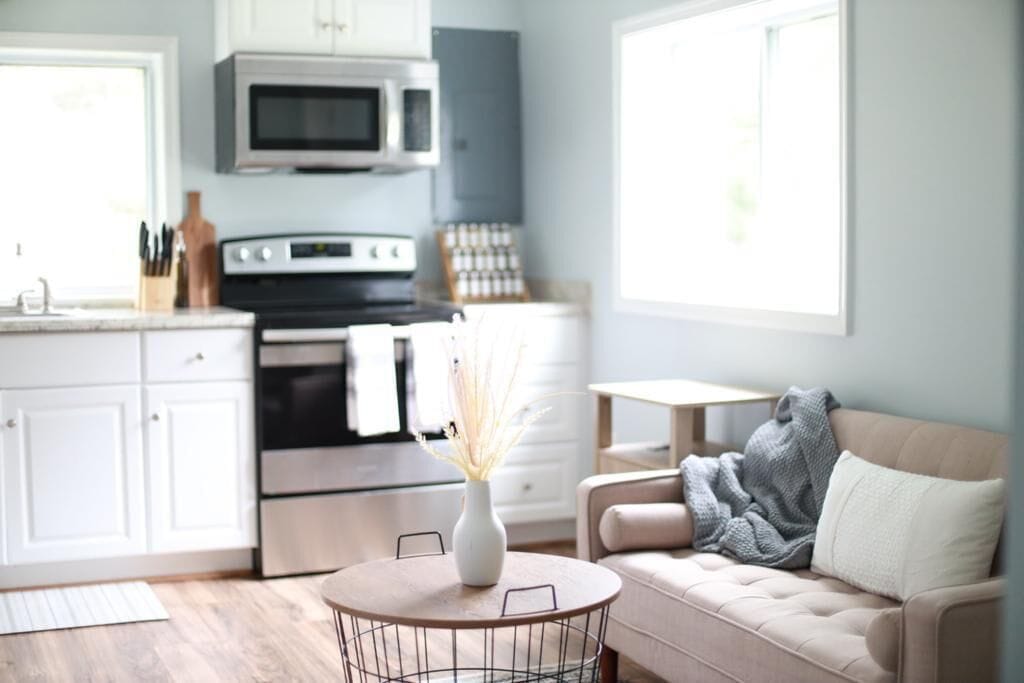 Une cuisine moderne avec des meubles blancs, un four à micro-ondes et une cuisinière. On y trouve un coin repas avec une table ronde et des chaises, ainsi qu'un canapé avec une couverture.