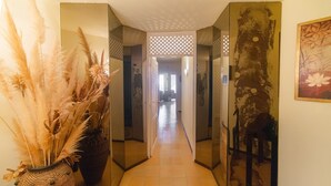 A hallway with a mirrored wall, a large vase with pampas grass, and a painting of a giraffe. - WELCS APARTMENT 284 PDA with terrace and view (Sant Feliu de Guixols)