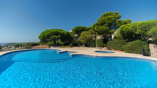 A clear blue swimming pool with a curved edge, surrounded by lush green trees and a clear sky. - WELCS APARTMENT 284 PDA with terrace and view (Sant Feliu de Guixols)