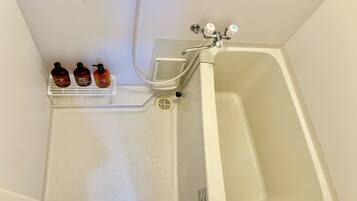 A bathroom with a bathtub, a shower, and a shelf with three bottles.