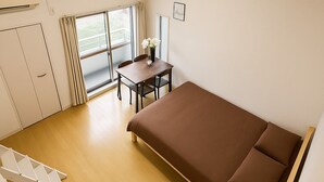 Una habitación pequeña con una cama, una mesa con sillas, una ventana con cortinas, una lámpara en el techo y un armario.