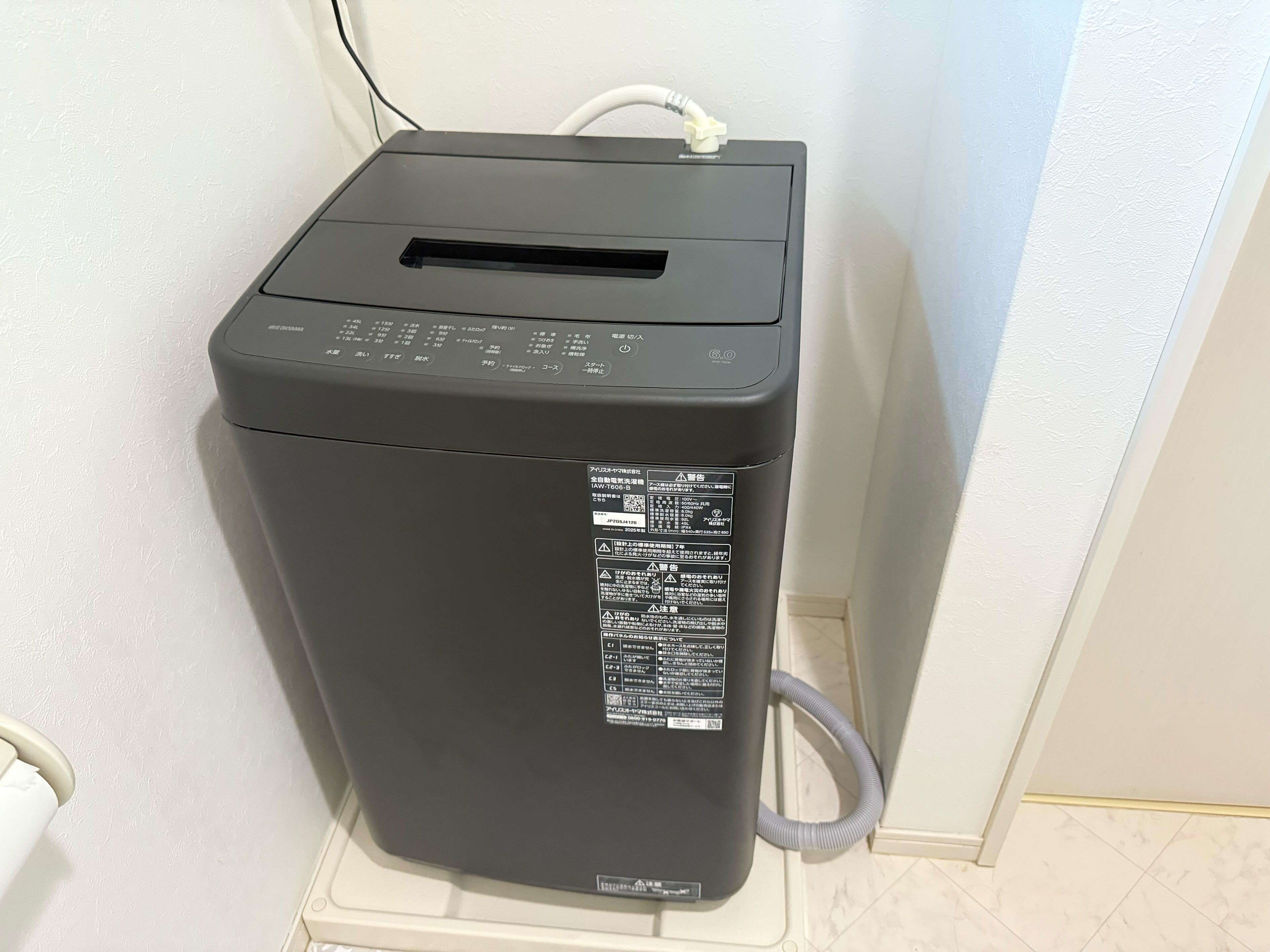 A compact, gray, wall-mounted laundry machine with a control panel and a QR code sticker.