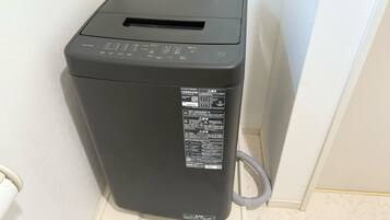 A compact, gray, wall-mounted laundry machine with a control panel and a QR code sticker.