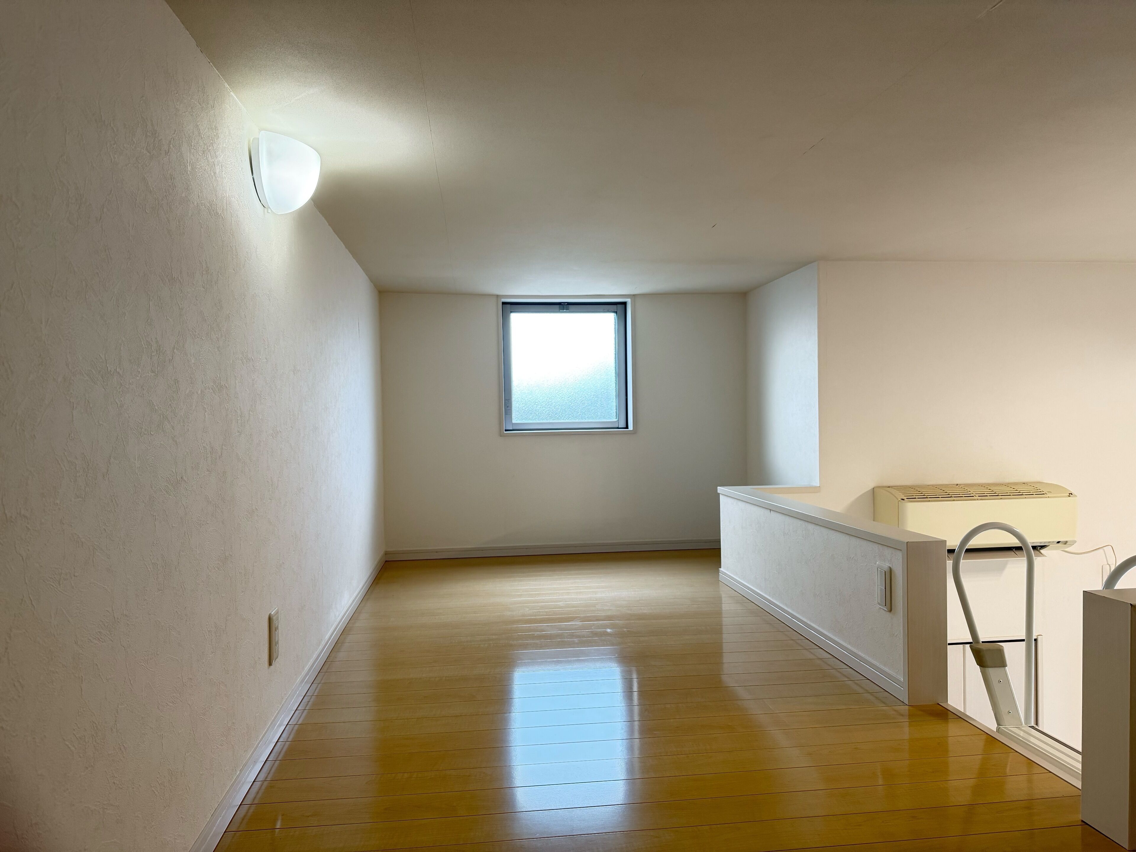 A narrow hallway with a wooden floor, a window, and a radiator.