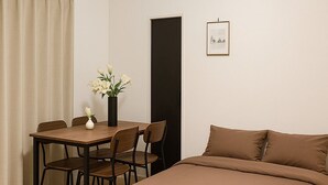 Un dormitorio con una cama, una mesa con sillas, un florero con flores y un cuadro en la pared.