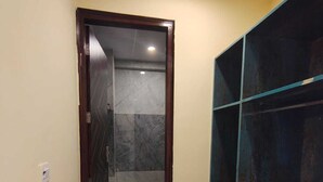 Un couloir étroit avec une porte donnant sur une salle de bain, un seau bleu et une étagère au revêtement foncé.