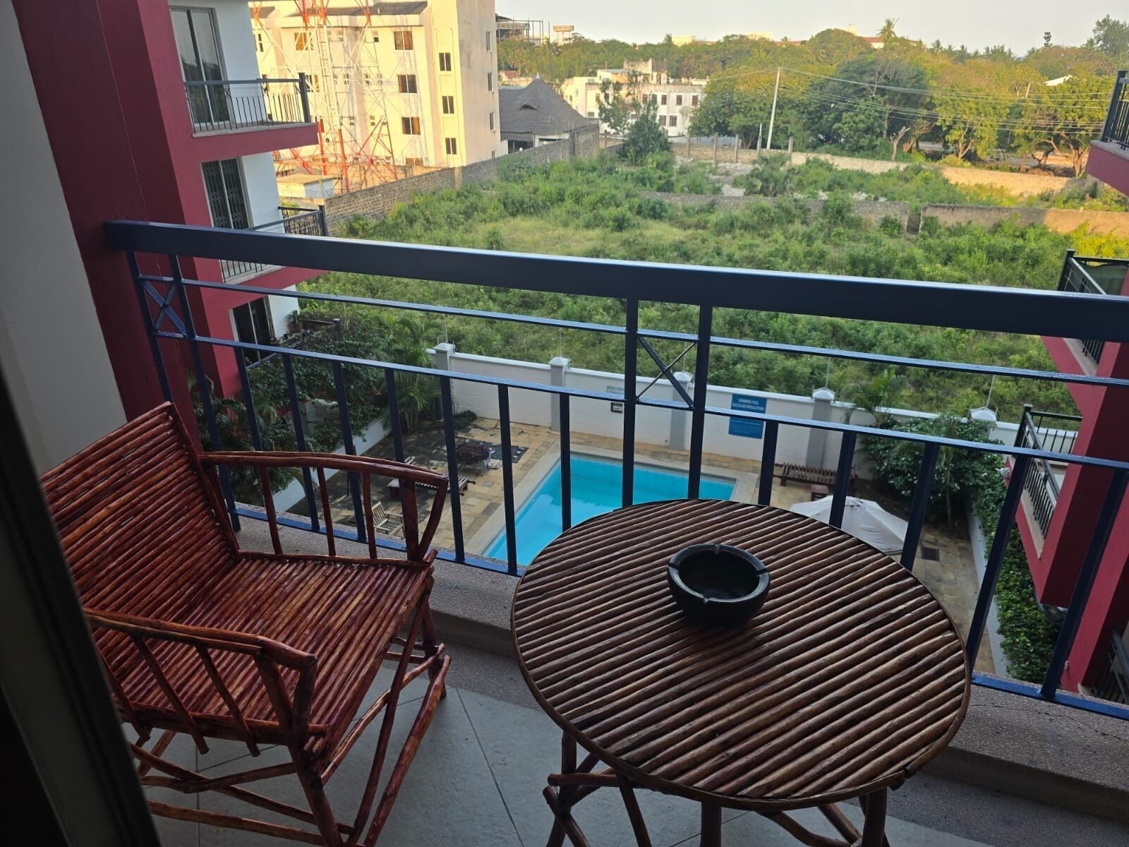 Ein Balkon mit zwei Holzstühlen und einem kleinen runden Tisch, mit Blick auf ein Schwimmbad und eine grüne Landschaft.