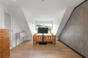 A bedroom with a wooden bed, a TV, and a window with a view of greenery. - Three Quarter Cottage (Bodinnick)