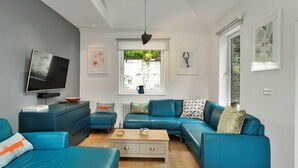 A modern living room with a sectional sofa, a flat-screen TV, and a coffee table. - Three Quarter Cottage (Bodinnick)