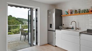 A modern kitchen with a built-in refrigerator, white cabinetry, and a wooden shelf above the sink. - Three Quarter Cottage (Bodinnick)