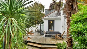 A modern house with a wooden deck, outdoor seating, and lush greenery. - Three Quarter Cottage (Bodinnick)