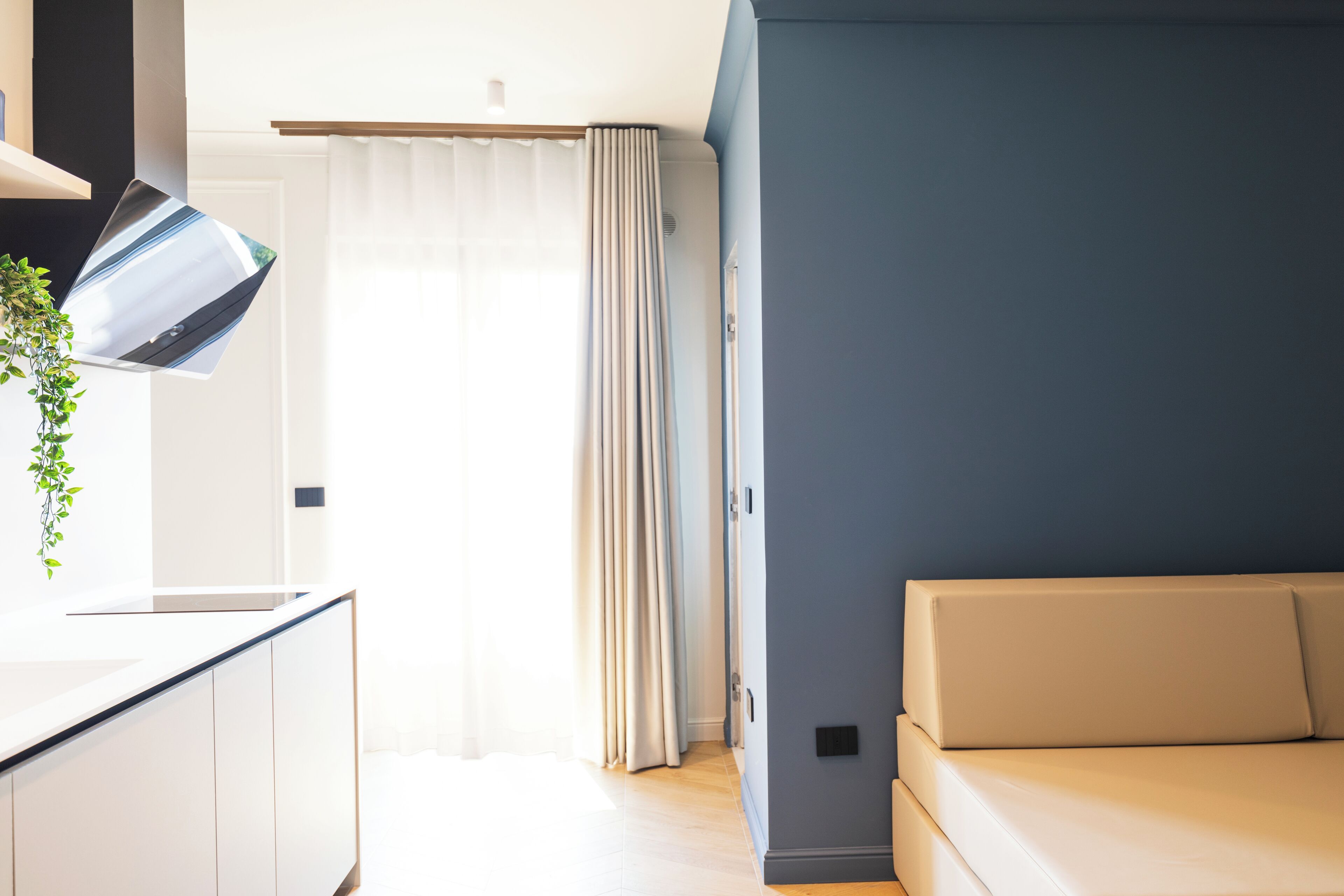 A modern living room with a sofa, a kitchen area with a counter, and a large window with curtains.