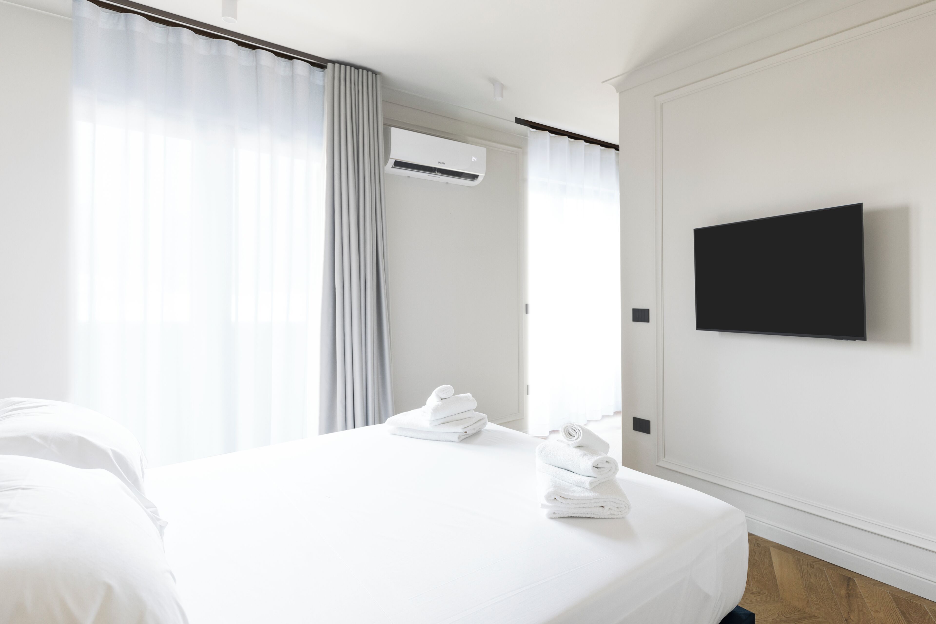 Una habitación de hotel moderna con una cama bien hecha, un televisor de pantalla plana montado y un equipo de aire acondicionado.