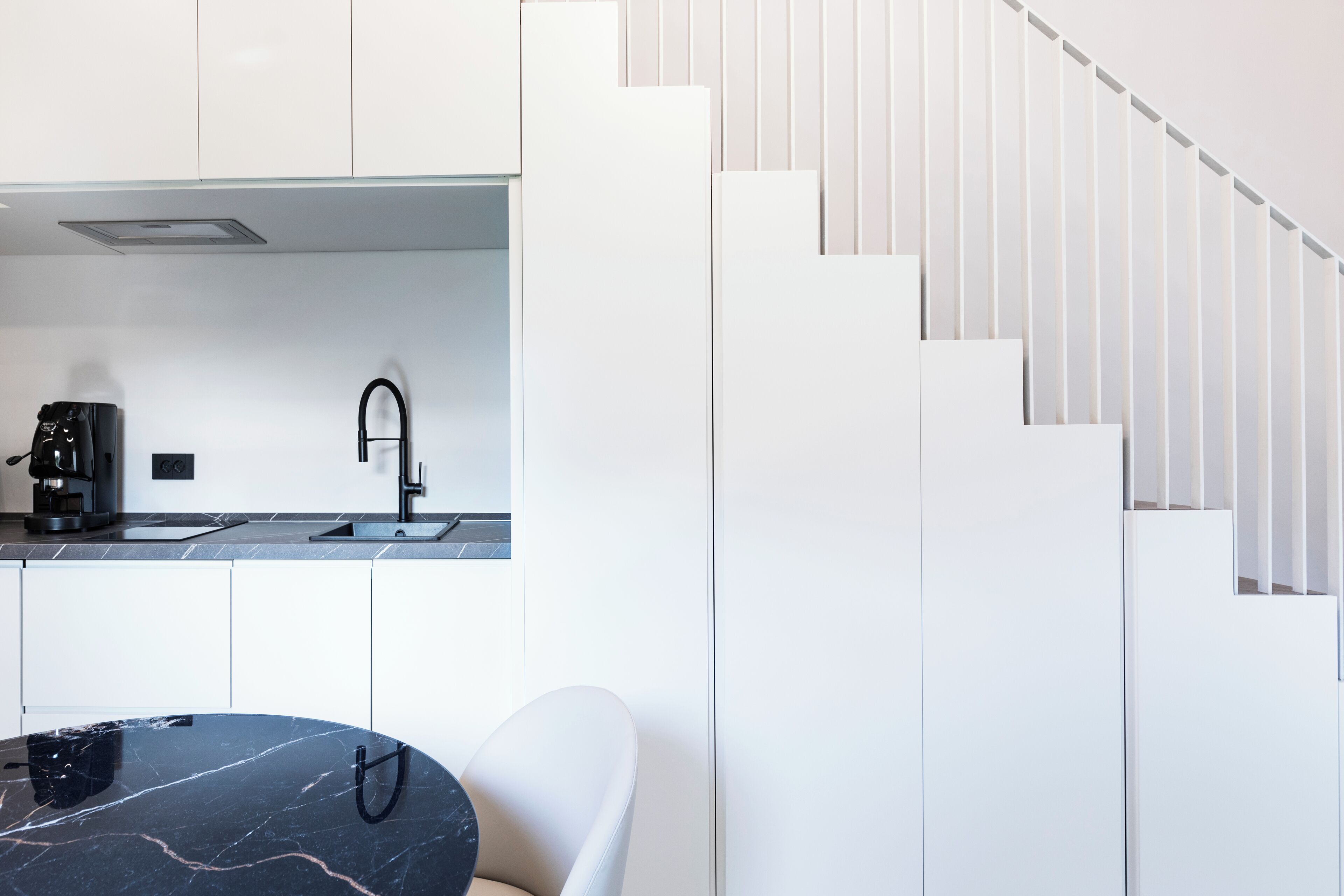 Une cuisine moderne avec des meubles blancs, une table en marbre noir et une chaise blanche.
