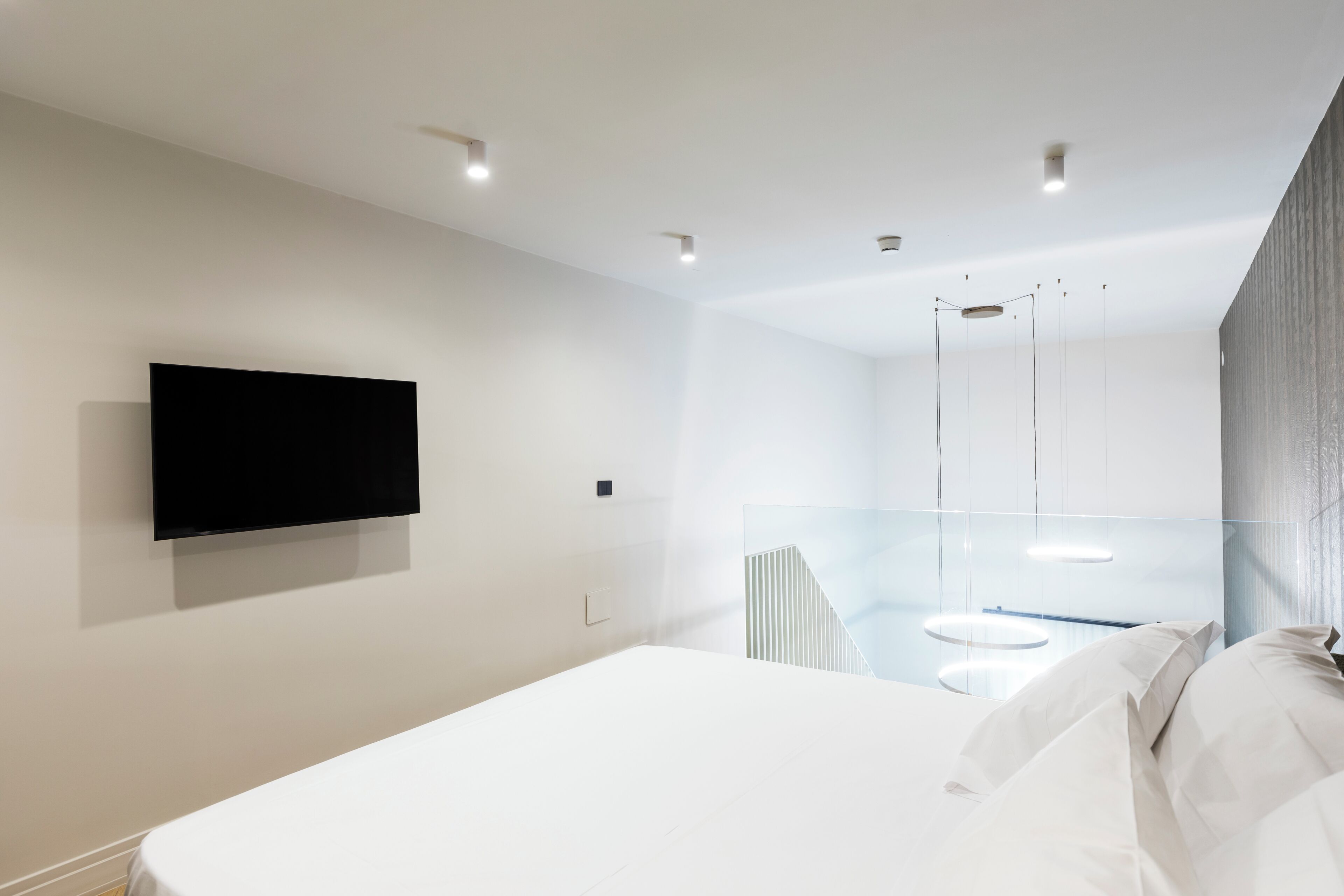 Una camera d'albergo moderna con un letto grande, una TV a parete e un divisorio in vetro che separa la zona notte dal bagno.