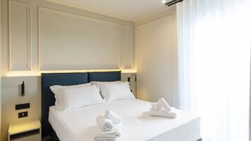 Cama bem arrumada com lençóis e toalhas brancos, cabeceira escura e mesa de cabeceira com abajur.