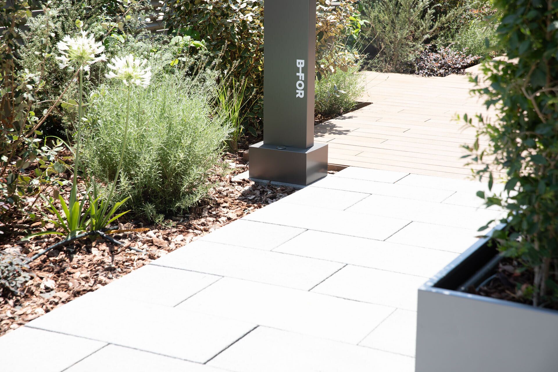 A pathway with a metal pillar labeled "BFOR" leading to a garden area with various plants and a wooden deck.