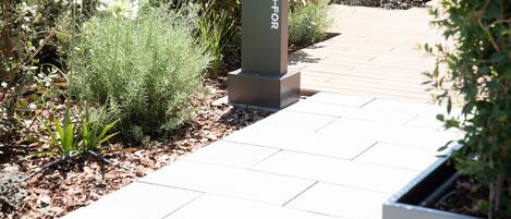 A pathway with a metal pillar labeled "BFOR" leading to a garden area with various plants and a wooden deck.