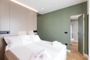 A modern hotel room with a neatly made bed, a green accent wall, and a visible bathroom with a shower. - Bfor Suite Experience (Nola)
