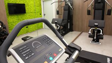 A gym with exercise equipment, a digital interface on the treadmill, and a green wall.