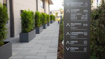 A directional sign with amenities including a reception snack area, camere rooms, palestra gym, lavanderia laundry, uscita exit, and piscina pool.