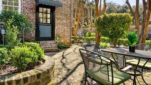 Un patio con un edificio de ladrillo, una ventana con persiana negra y una mesa con sillas.