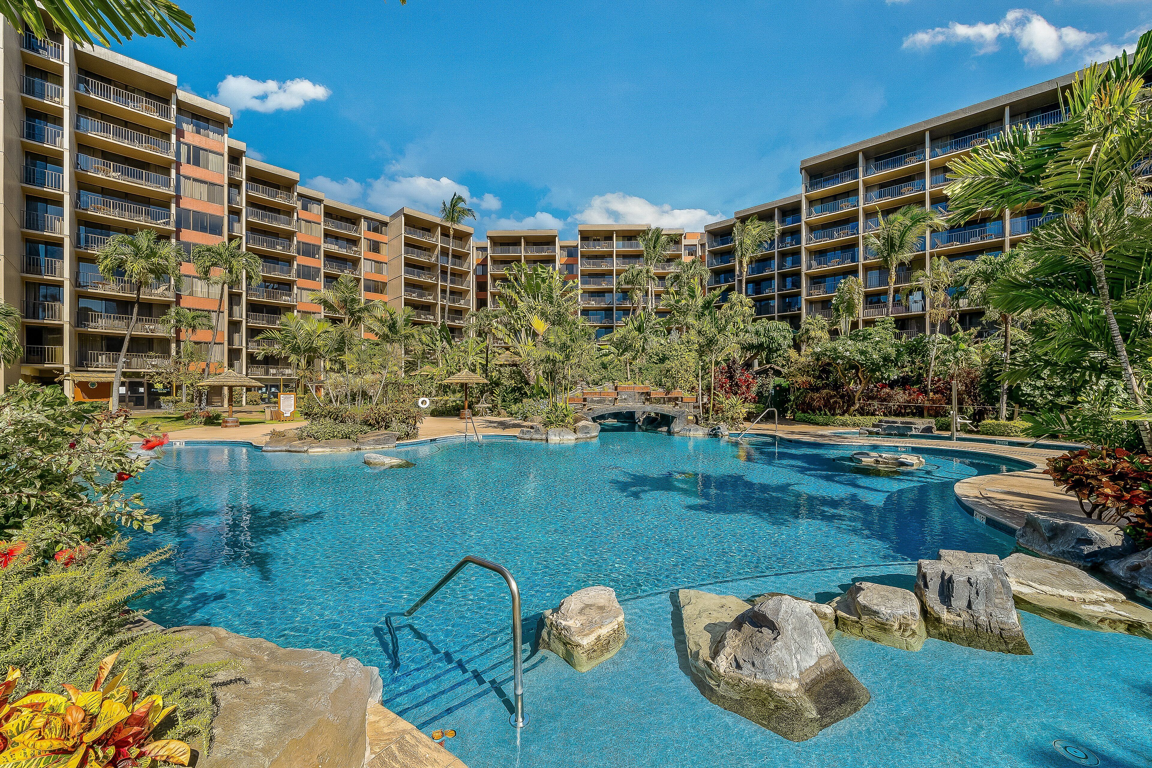 Ein Hotel mit mehreren Balkonen, einem Pool mit Felsen und tropischer Bepflanzung.