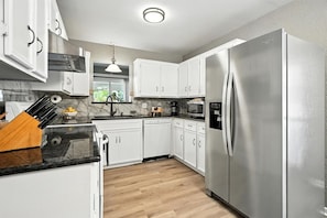 A modern kitchen with white cabinets, a stainless steel refrigerator, and a wooden countertop.