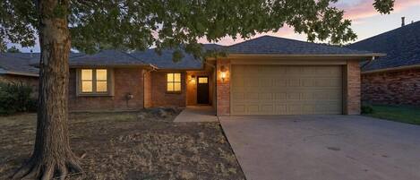 A residential house with a garage, a driveway, and a tree in the foreground.