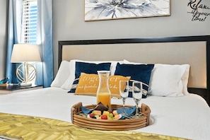 A neatly made bed with a tray of fruit and juice, two glasses, and a pillow with a message.