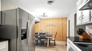 Una cocina moderna con un refrigerador de acero inoxidable, una mesa de comedor con sillas y una pared decorativa de madera.