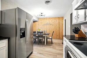 A modern kitchen with a stainless steel refrigerator, a dining table with chairs, and a wooden accent wall.