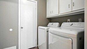 Un cuarto de lavandería con puerta cerrada, dos lavadoras y un armario sobre las máquinas.