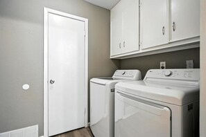 A laundry room with a closed door, two washing machines, and a cabinet above the machines.