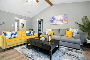 A living room with a yellow sofa, a grey sofa, a coffee table, and a painting on the wall.