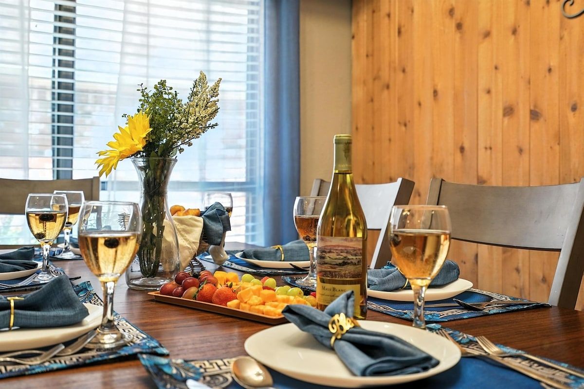 Une table à manger dressée avec des assiettes, des verres, une bouteille de vin et un plateau de fruits.