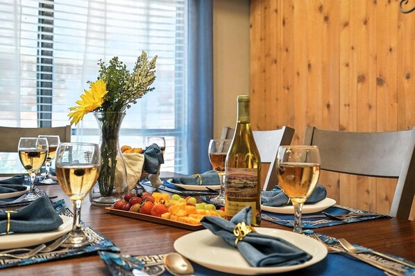 Una mesa de comedor dispuesta con platos, vasos, una botella de vino y una bandeja de frutas.