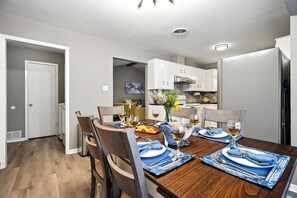 A dining area with a wooden table set for four, chairs, and a kitchen in the background.