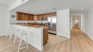 A modern kitchen with wooden cabinets, a stainless steel refrigerator, and a white countertop.