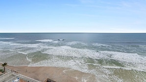 A beach view with waves, a sandy shore, and a railing.