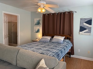 A bedroom with a bed, a ceiling fan, a door, and a wall-mounted artwork. - Eleven South: One - Modern Studio Apartment (Abilene)