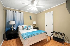 A bedroom with a bed, two bedside tables, a ceiling fan, a door, and a black metal rack. - The Inland Tide 3 bedrooms • 2 bath  • Entire home (Abilene)