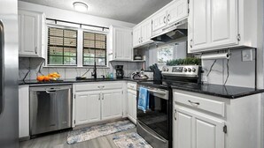 A kitchen with white cabinets, a stainless steel dishwasher, a black countertop, and a blue towel hanging on the oven handle. - The Inland Tide 3 bedrooms • 2 bath  • Entire home (Abilene)